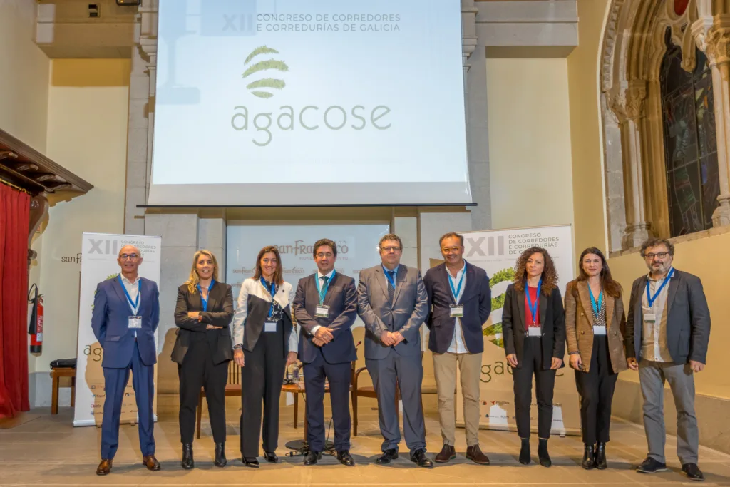Foto de grupo en el escenario del XII Congreso de Agacose celebrado en el Hotel Monumento San Francisco de Santiago de Compostela, con destacados miembros y logotipos del evento.