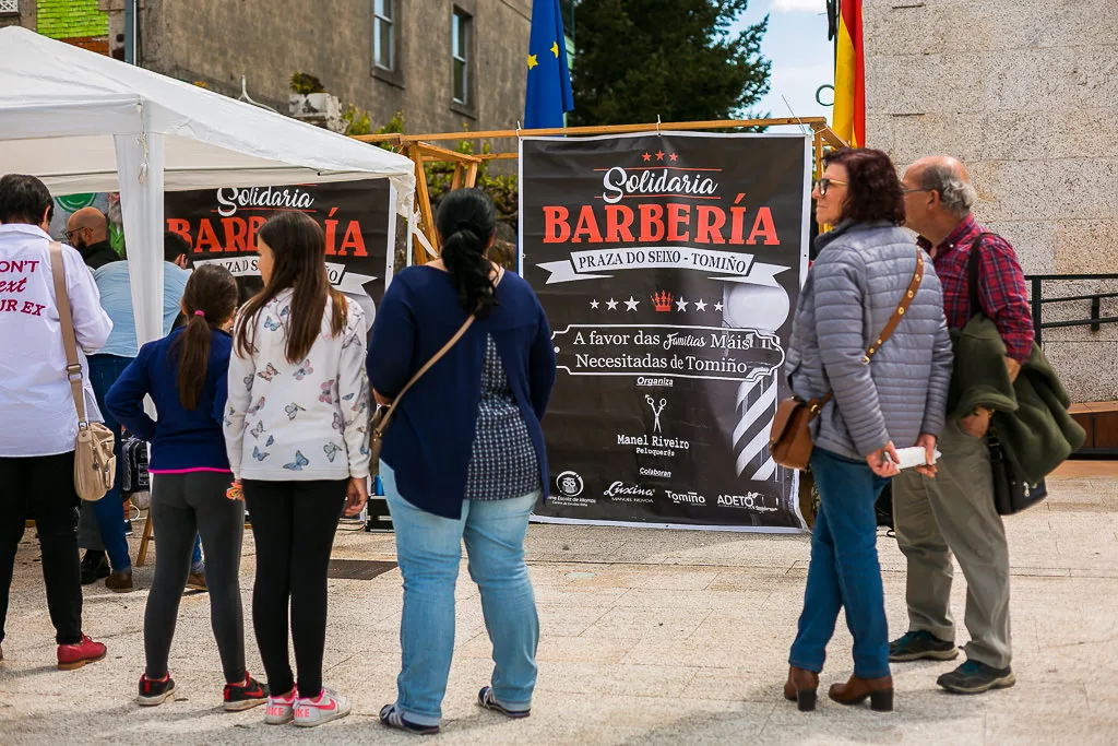 Fotografía para eventos solidarios en Galicia: carpa del Barbero Solidario en la Plaza del Ayuntamiento de Tomiño, con varias personas esperando su turno para cortes y afeitados solidarios a cargo de Manel Riveiro