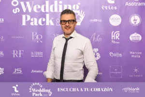 Richard Candendo, fotógrafo de Whitebox Portraits, posando en el photocall del Wedding Pack Solidario – Cásate no Camiño, con el banner del evento de fondo y el lema "Escucha tu corazón".